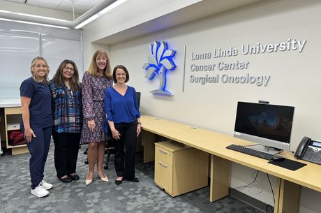 Four women stand to the left and pose next to a wall sign reading &quot;Loma Linda University Cancer Center Surgical Oncology&quot;